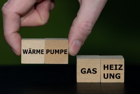 Wärmepumpe oder Gasheizung Eine Hand setzt Holzwürfel mit Wörtern zusammen, sie bilden die Worte "Wärme-Pumpe" und "Gas-Heizung"