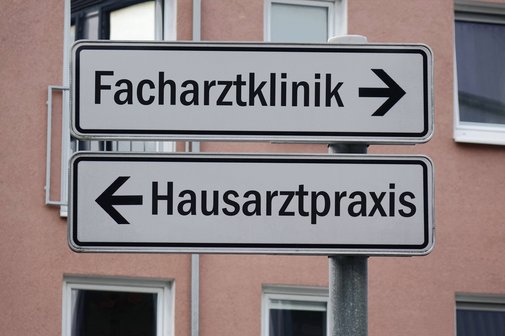 Ein Wegweiser mit zwei Schildern. Der eine zeigt nach rechts mit der Aufschrift "Facharztklinik", der andere nach links mit der Aufschrift "Hausarztpraxis"