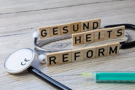 Holzbuchstaben bilden das Wort "Gesundheitsreform". Daneben liegt ein Stethoskop.