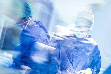Verschwommene Aufnahme zweier männlicher Chirurgen während einer Operation, sie tragen blaue OP-Kleidung