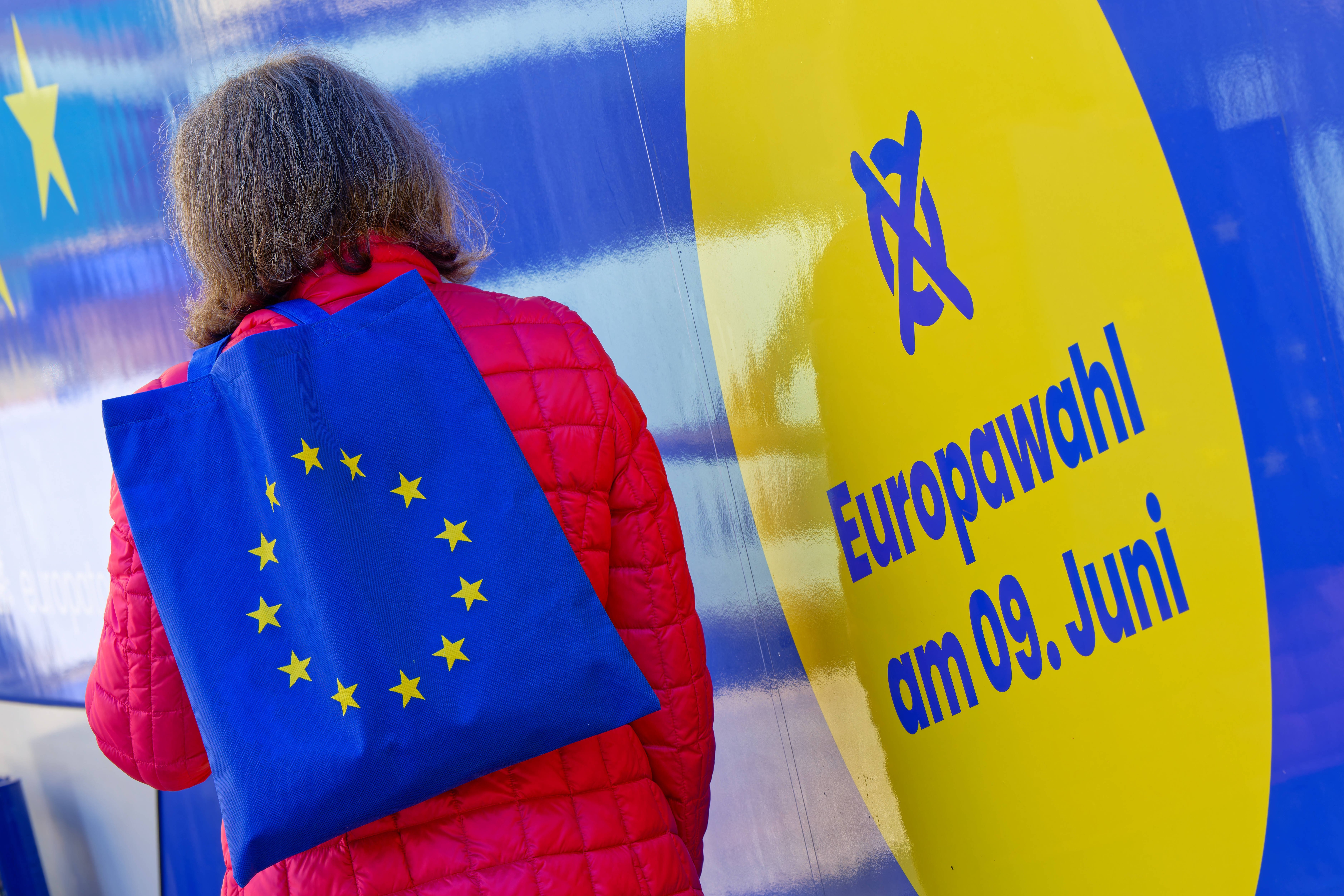 Europawahl am 9. Juni Eine Frau mit einer Tasche, die als Aufdruck die Flagge der Europäischen Union hat, steht vor einem blau-gelben Plakat mit der Aufschrift "Euriopawahl am 9. Juni".