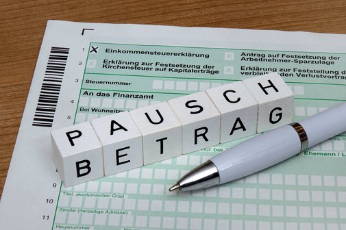 Behindertenpauschbetrag Ein Steuerformular für die Einkommensteuererklärung, darauf liegen Buchstabenwürfel, die das Wort "Pauschbetrag" bilden, und ein Kugelschreiber