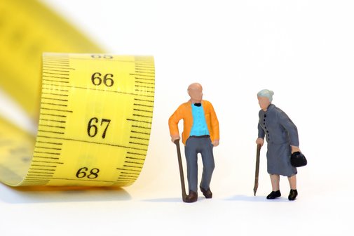 Zwei Rentner-Fig&uuml;rchen - ein Mann und eine Frau - vor einem gelben Ma&szlig;band, auf dem die Zahlen 66, 67 und 68 zu sehen sind.