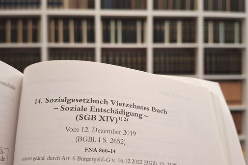Ein aufgeschlagenes SGB 14, im Hintergrund sieht man Regale mit Fachb&uuml;chern.