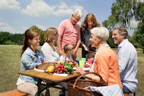 Unterschiedliche Menschen - alt und jung, M&auml;nner und Frauen, mit und ohne Behinderung - sitzen drau&szlig;en auf Bierb&auml;nken an einem Tisch, essen gemeinsam.