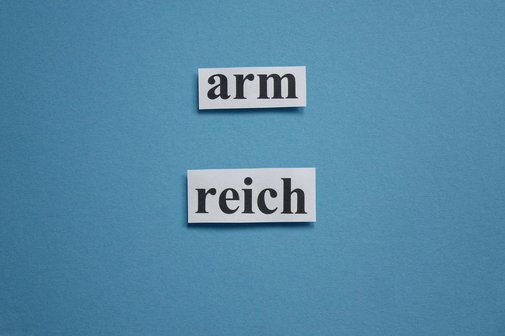 Ungleiche Vermögensverteilung Auf blauem Grund stehen die Wörter "arm" und "reich" aus ausgeschnittenem Papier
