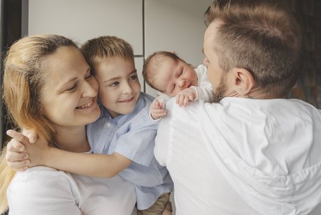 Weltfrauentag und Gleichberechtigung Eine Familie steht eng zusammen, die Mutter hat eine kleinen Jungen auf dem Arm, der Vater ein wenige Wochen altes Baby.