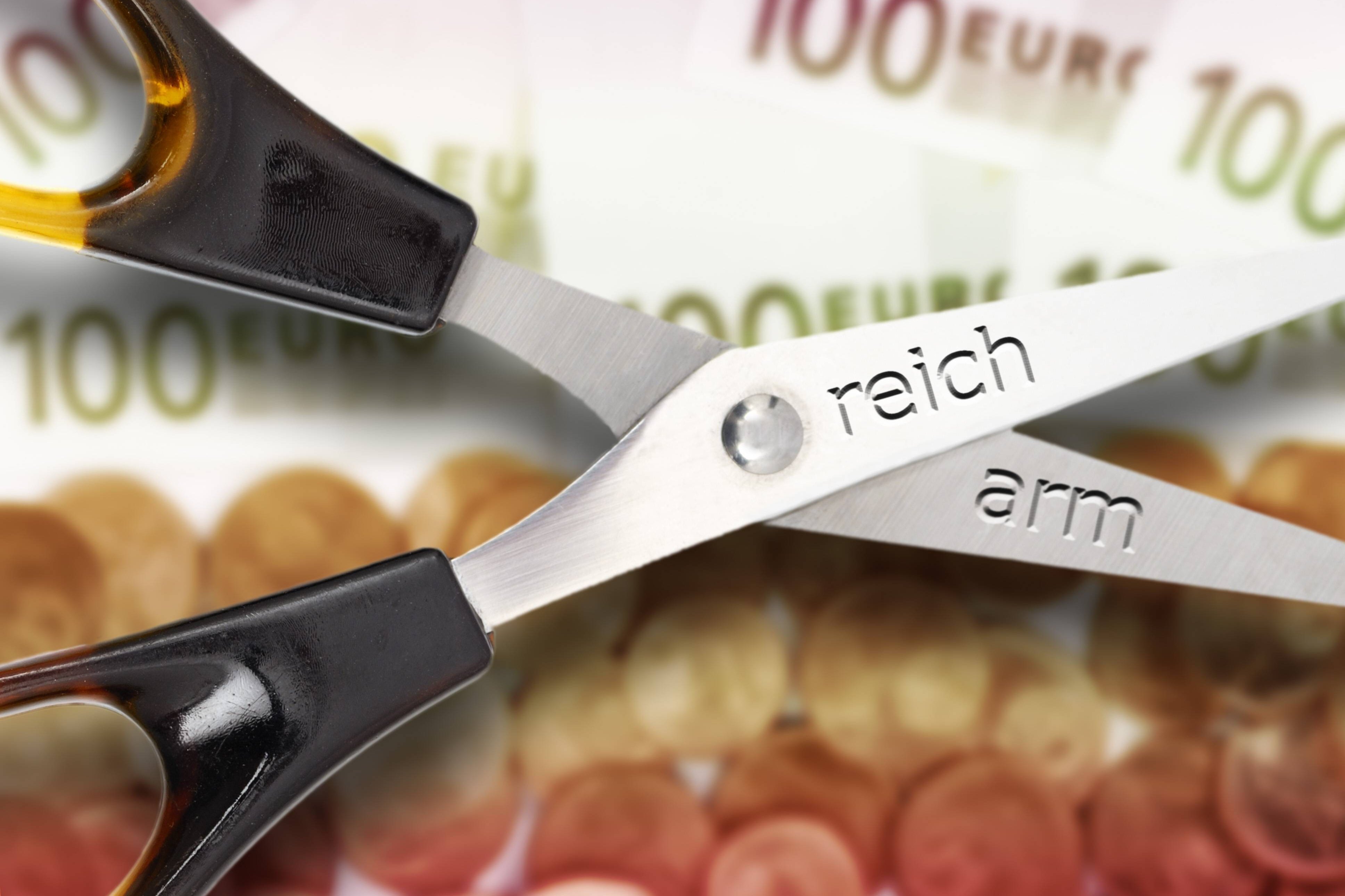 Schere zwischen Arm und Reich Das Symbolbild zeigt eine Schere mit geöffneten Scherenblättern; auf dem einen steht "reich", auf dem anderen "arm". Im Hintergrund sieht man Geldscheine und -münzen.