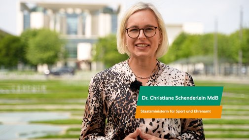 Christiane Schenderlein, Staatsministerin für Ehrenamt und Sport, spricht in die Kamera. Hinter ihr ist das Bundeskanzleramt zu sehen.