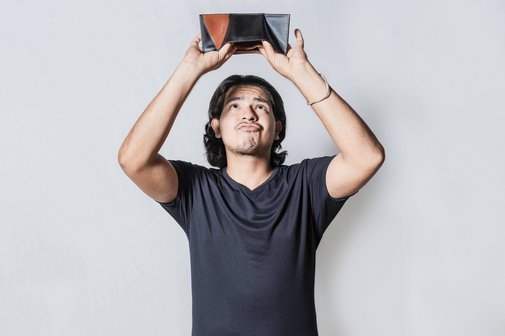 Ein Mann hält seine leere Brieftasche umgedreht über den Kopf, er schaut mit traurigem Gesichtsausdruck, ob etwas herausfällt.