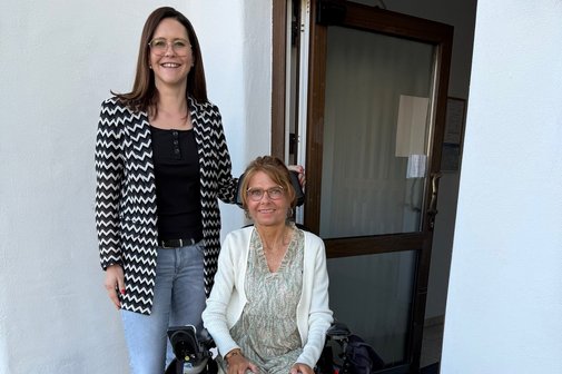 Manuela Ernst, im Rollstuhl, und Franziska Geiß stehen nebeneinander vor einer Tür mit elektrischem Türantrieb.