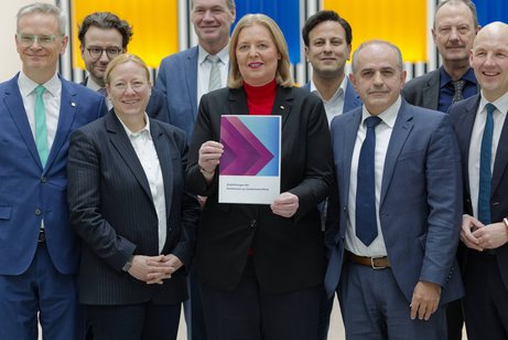 Gruppenbild: Bärbel Bas (SPD), Bundesministerin für Arbeit und Soziales, hält den Abschlussbericht der Kommission zur Sozialstaatsreform in die Kamera. Die Mitglieder der Kommission stehen um sie herum.