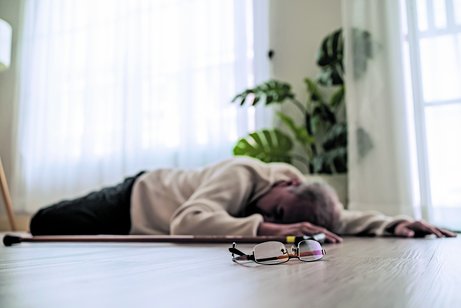 Ein ältere Person ist gestürzt und liegt hilflos auf dem Fußboden einer Wohnung.
