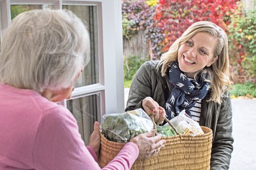 Eine Nachbarin bringt einer &auml;lteren Dame einen Korb mit Lebensmitteln.