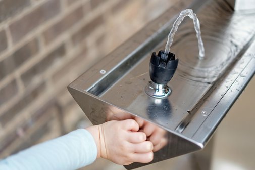 Ein Kind nutzt einen Trinkwasserspender um seinen Durst zu stillen.