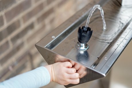 Ein Kind nutzt einen Trinkwasserspender um seinen Durst zu stillen.