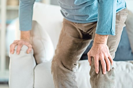 Ein &auml;lterer Mann st&uuml;tzt sich beim Aufstehen auf ein Sofa ab.
