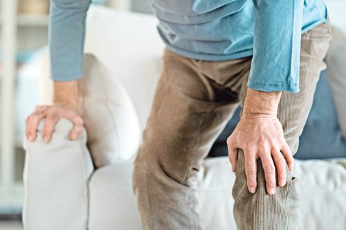 Ein &auml;lterer Mann st&uuml;tzt sich beim Aufstehen auf ein Sofa ab.