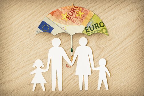 Familiensilhouette aus Papier mit Regenschirm aus Euro-Banknoten auf Holzgrund.