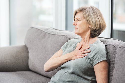 Eine &auml;ltere Frau mit Schmerzen in ihrem Wohnzimmer&ndash; ein Notfall auf dem Sofa. 