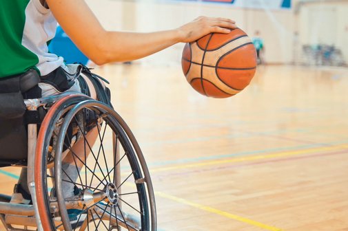 Ein Basketballspieler im Rollstuhl schlägt einen Ball.