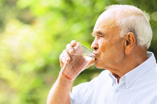 Ein älterer Mann trinkt aus einem Wasserglas.