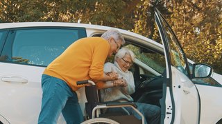 Ein Mann hilft einer Frau mit Behinderungen aus dem Auto.