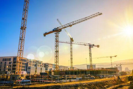 Große Baustelle mit mehreren Kränen, die an einem Gebäudekomplex arbeiten, mit klarem blauen Himmel.