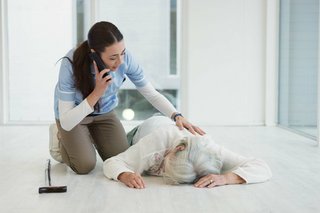 Das Bild zeigt einen Sturzunfall. Eine ältere Frau liegt am Boden. Eine jüngere Frau kniet neben ihr und telefoniert um Hilfe.