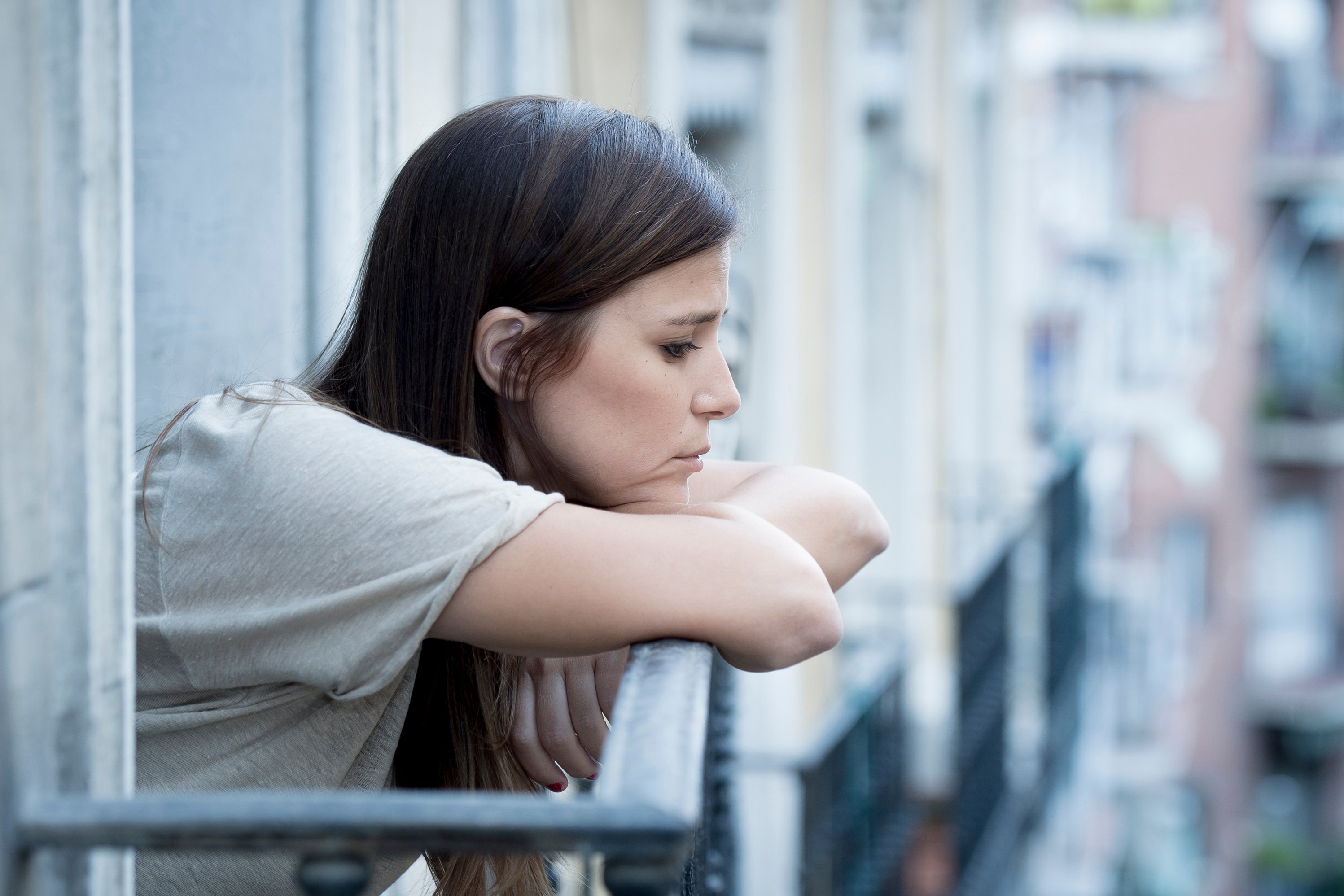 Eine junge Frau, die an Depressionen leidet und besorgt auf ihrem Balkon sitzt.