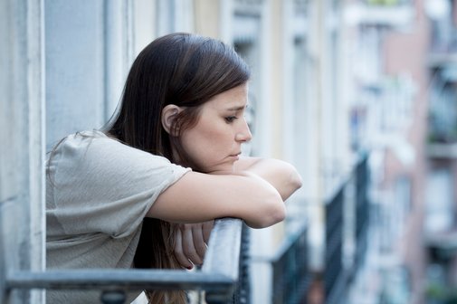 Eine junge Frau, die an Depressionen leidet und besorgt auf ihrem Balkon sitzt.