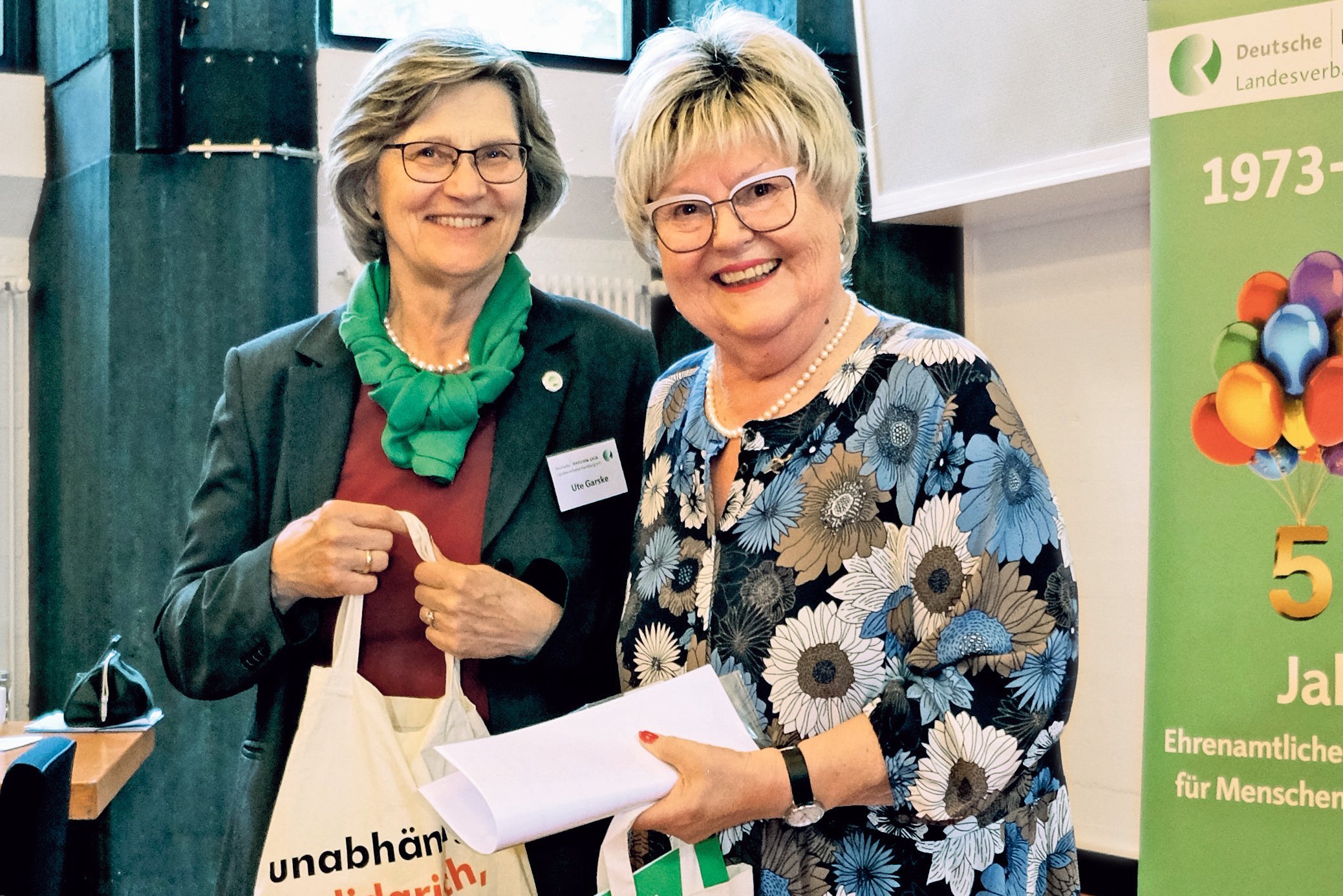 Im Bild zu sehen: Frau Garske und Frau Schommer vor einem Plakat der Rheuma-Liga.