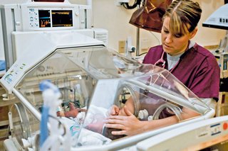 Das Bild zeigt eine Krankenschwester am Brutkasten bei der Frühgeborenenpflege.