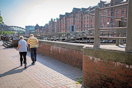 Zwei ältere Menschen laufen in der Speicherstand an einem Kanal entlang.