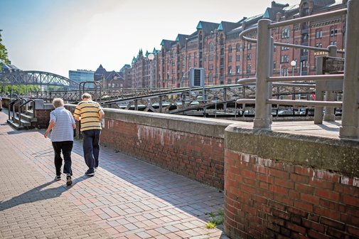 Zwei ältere Menschen laufen in der Speicherstand an einem Kanal entlang.