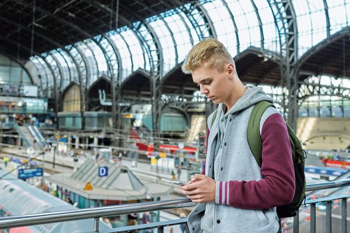 Ein Jugendlicher checkt in einem Bahnhof per Mobiltelefon die Fahrpläne.