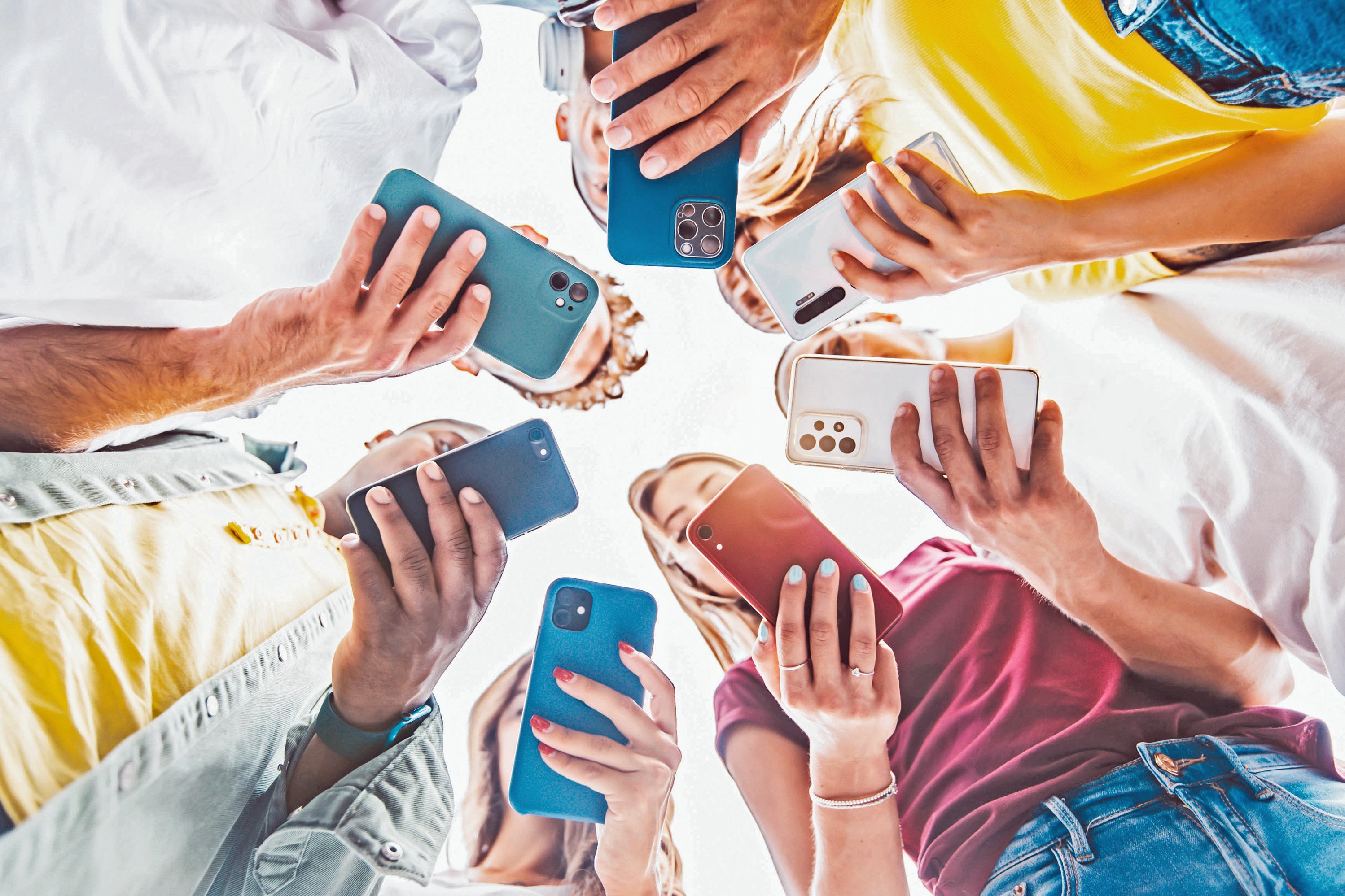 Sieben Jugendliche stehen im Kreis und blicken auf ihr eignes Smartphone.