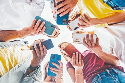 Sieben Jugendliche stehen im Kreis und blicken auf ihr eignes Smartphone.