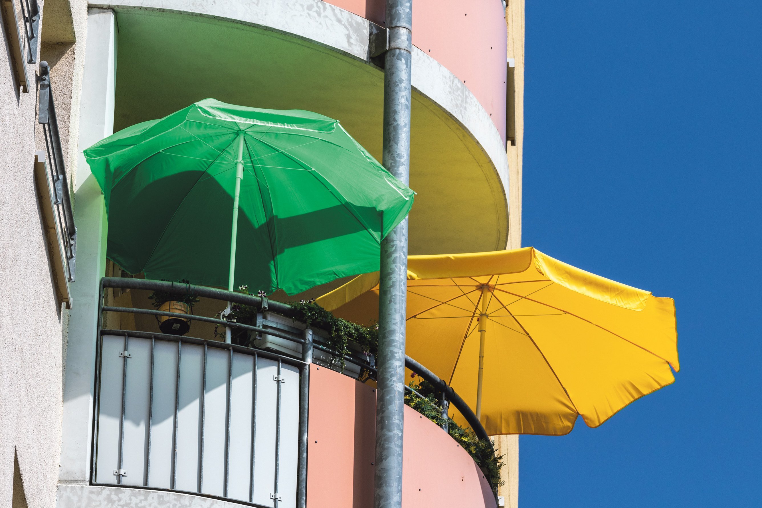 Ein Balkon mit zwei aufgespannten großen Sonnenschirmen.