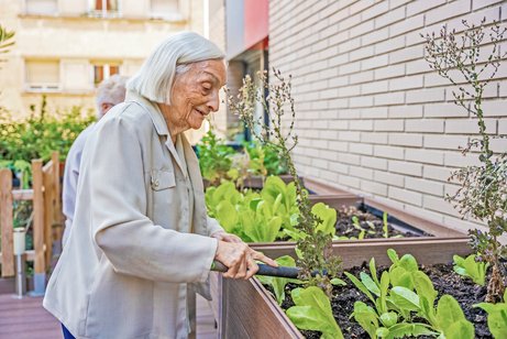 Wie findet man das richtige Pflegeheim Frau pflegt Pflanzen in einem Hochbeet in einem Seniorenheim.