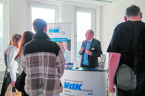 Vor Herrn Kutschkau und vor dem VdK-Infostand stehen interessiert zuhörende Menschen.