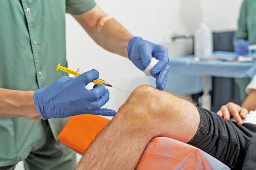 Medizinische Injektion am Knie. Arzt hält Spritze zur Injektion ins Knie.