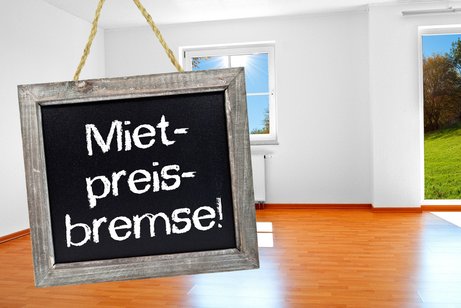 Kreidetafel mit Mietpreisbremse, platziert in einer leeren Wohnung.