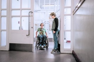 Eine Hilfsperson öffnet einer Frau im Rollstuhl eine große Tür.