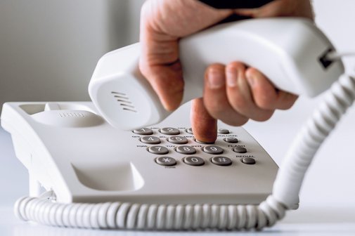 Das Bild zeigt, wie eine Person an einem Telefon die Nummer eintippt und den Hörer dabei in der Hand hält.