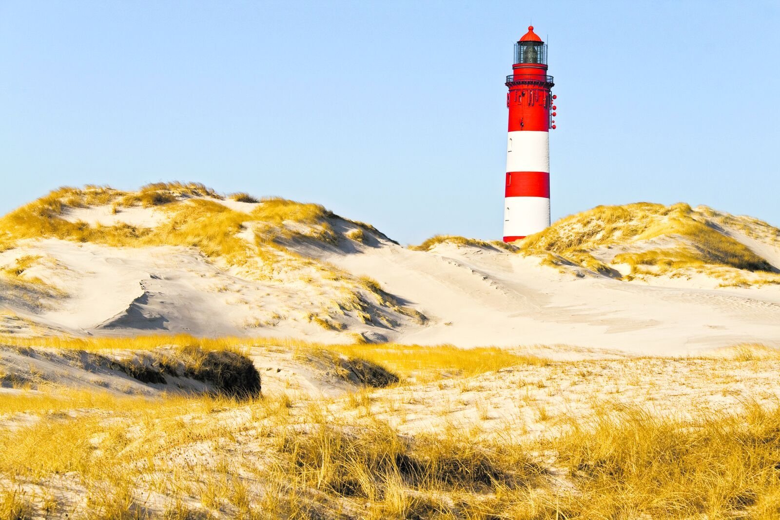 In einer Dünenlandschaft steht ein Leuchtturm und alles vermittelt Entspannung. 