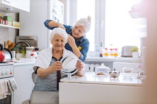 Einer älteren Frau werden in der Küche die Haare geschnitten.
