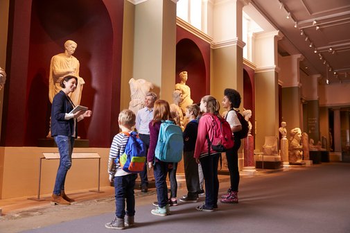 Schülerinnen und Schüler und Lehrerin bei einem Schulausflug ins Museum mit Führerin.