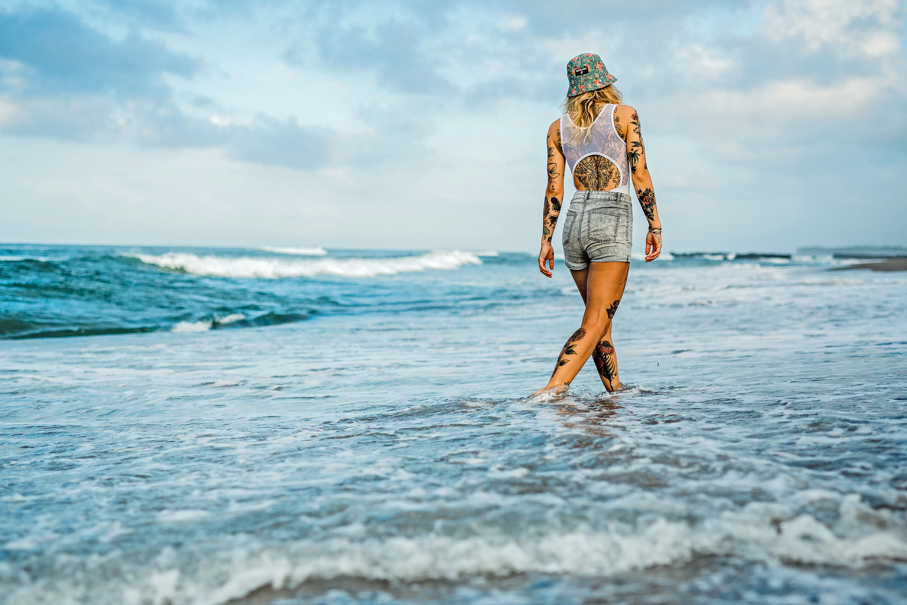 Tattoos und Vorsorge Eine am ganzen Körper tätowierte Frau genießt den Strand und das Wasser an ihren Füßen.