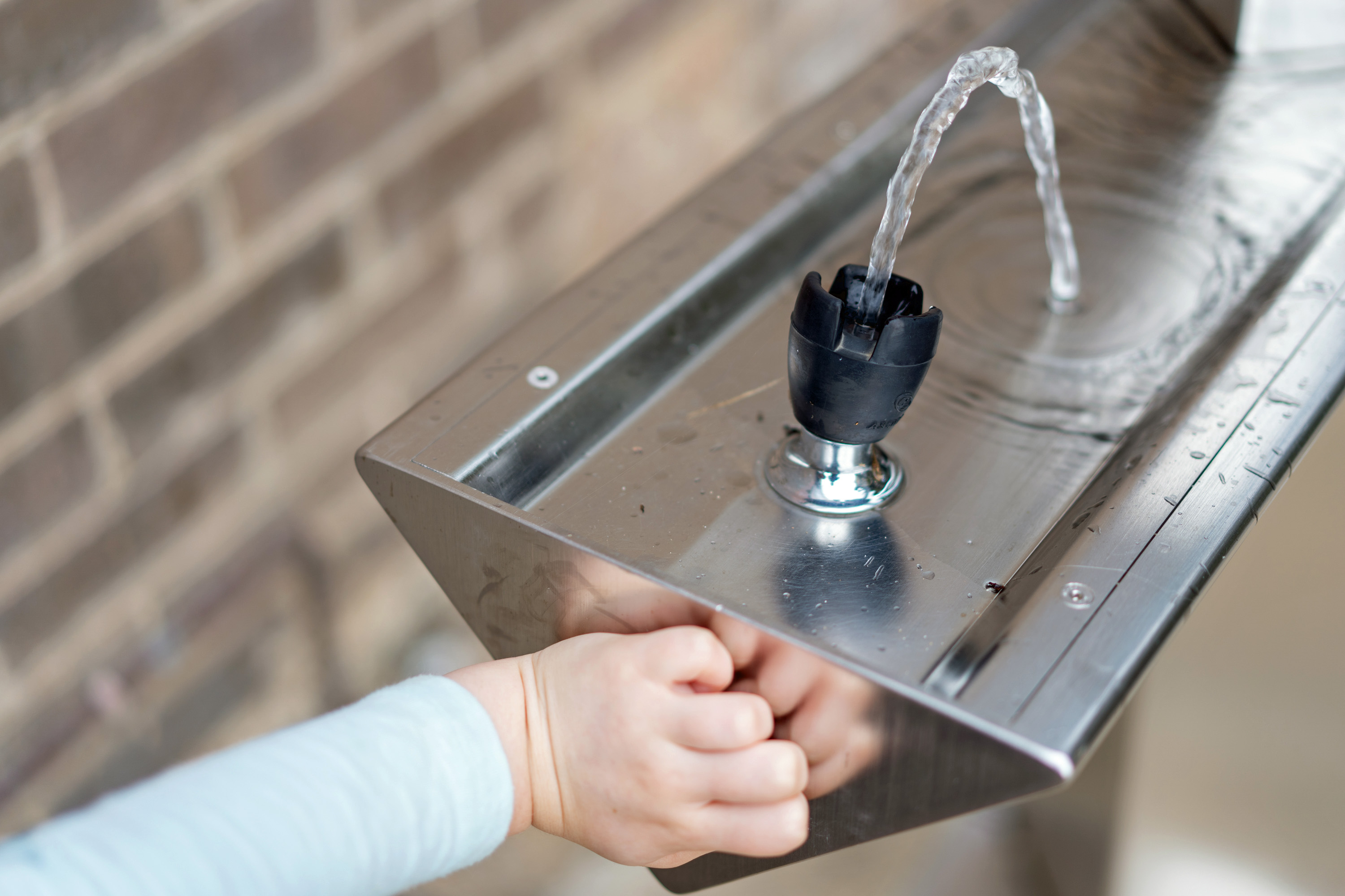 Ein Kind nutzt einen Trinkwasserspender um seinen Durst zu stillen.